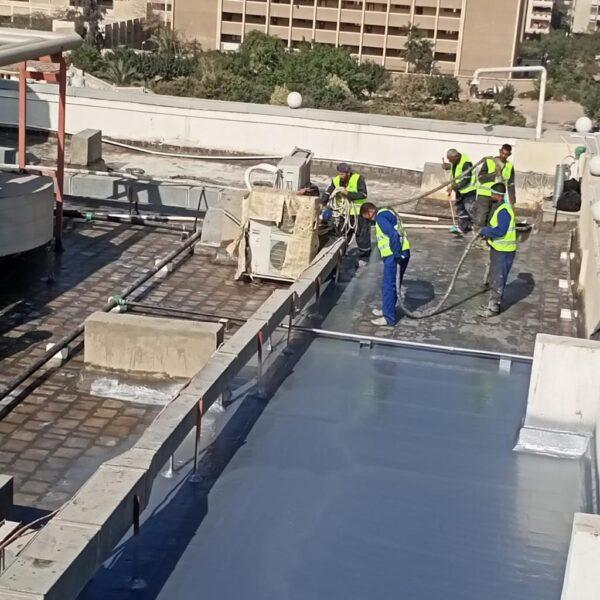 رجل يرتدي زيّ عمال يرش مادة البولي يوريا على سطح باستخدام خرطوم خاصّ.